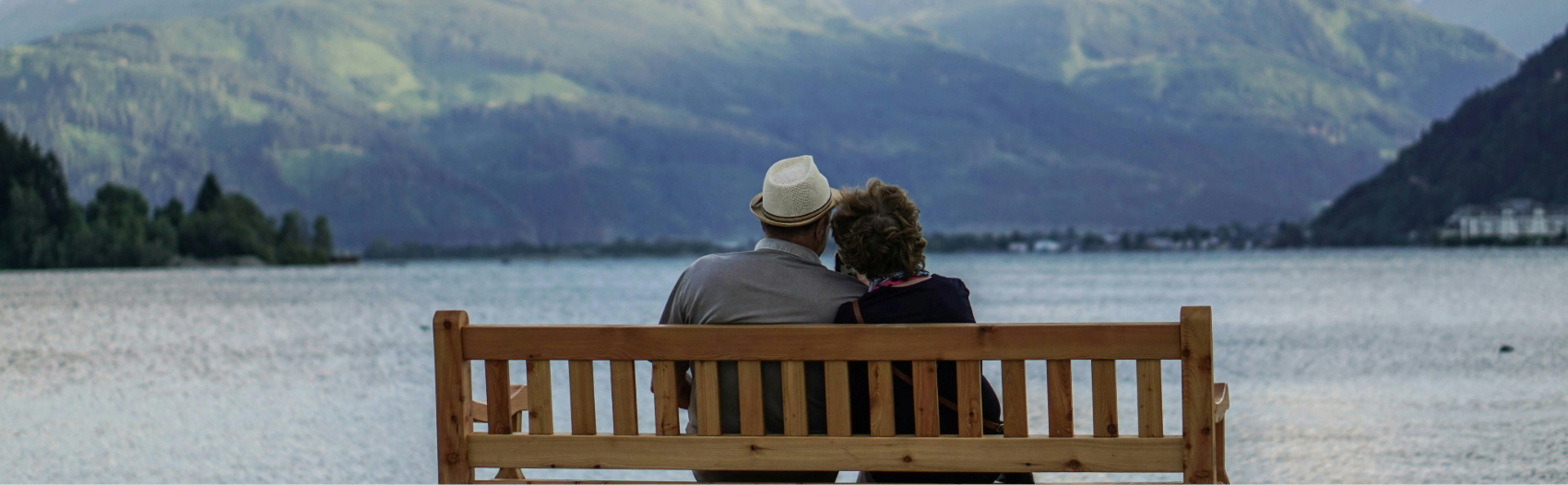 A couple ready for a retirement life coach sits on a bench looking out on a lake by a mountain